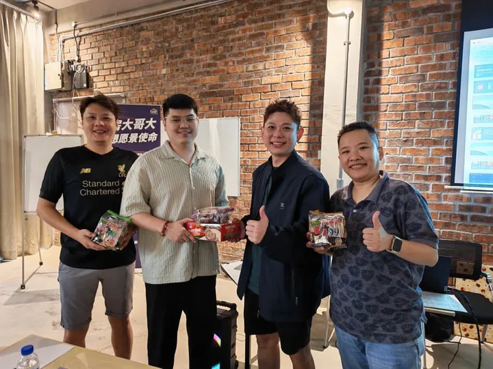 Four people posing indoors while holding small gift packages.