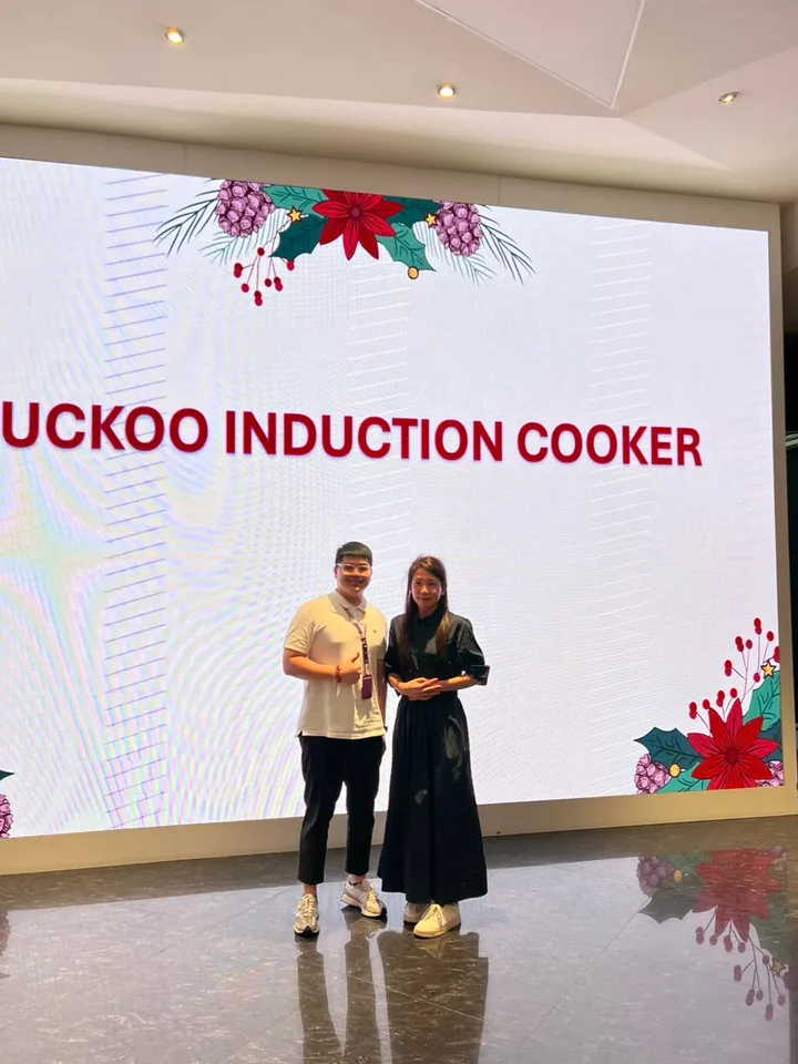 Two people standing on stage in front of a large induction event display.