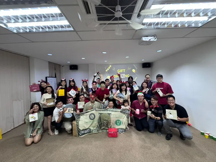 A group holding gifts and festive props in front of a gift-opening display.