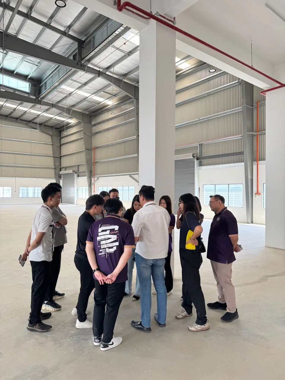 A group standing in a circle and talking inside a high-roof industrial space.