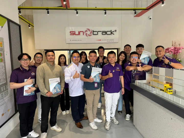 A group holding brochures beside a building model in an indoor showroom.