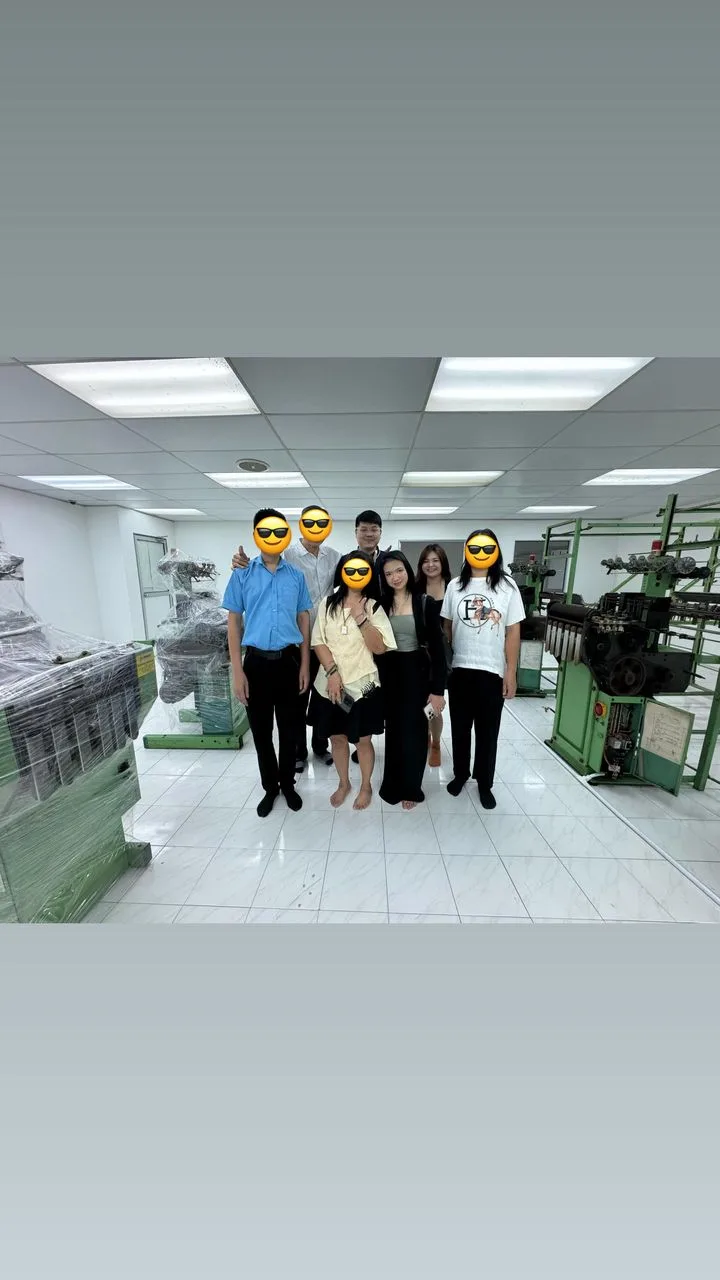 A group posing between rows of industrial equipment, with several faces covered by emoji.
